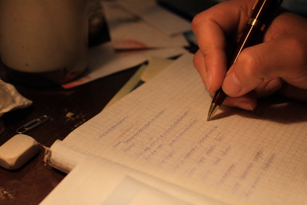 Main écrivant des conjugaisons dans un cahier